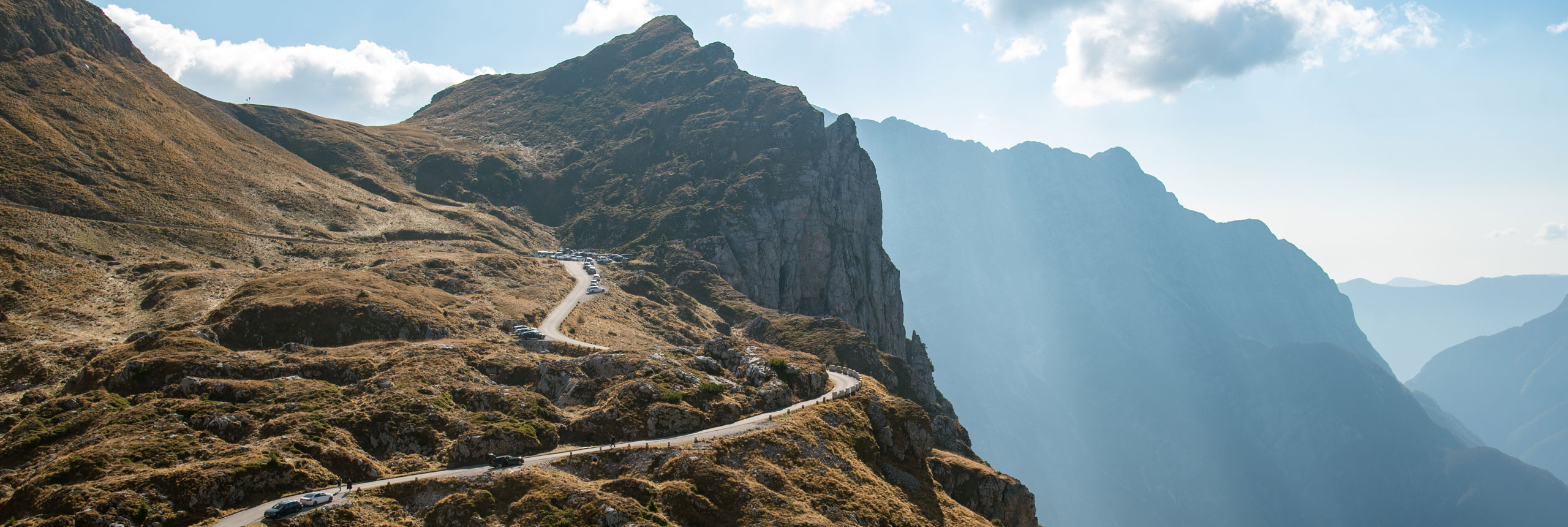 Fanad Head Lighthouse with surrounding cottages on a grassy cliff overlooking a blue ocean, with green hills and sandy beaches in the background.
